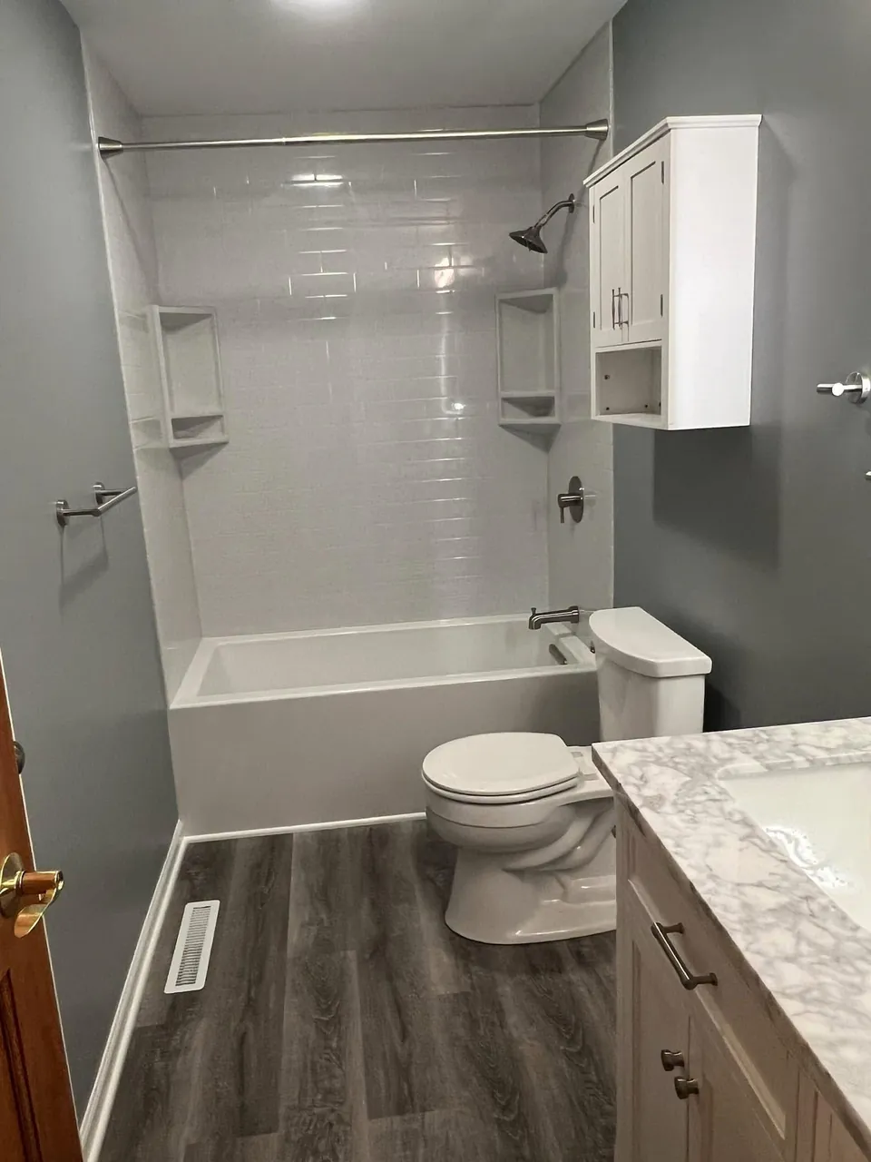 Bathroom with a white tub and shower surround, vanity, and wood-look flooring