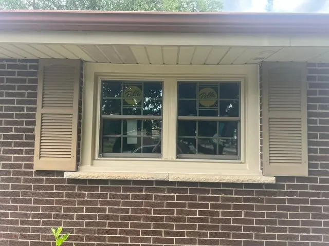 Wide window with white trim and shutters set into a brick exterior