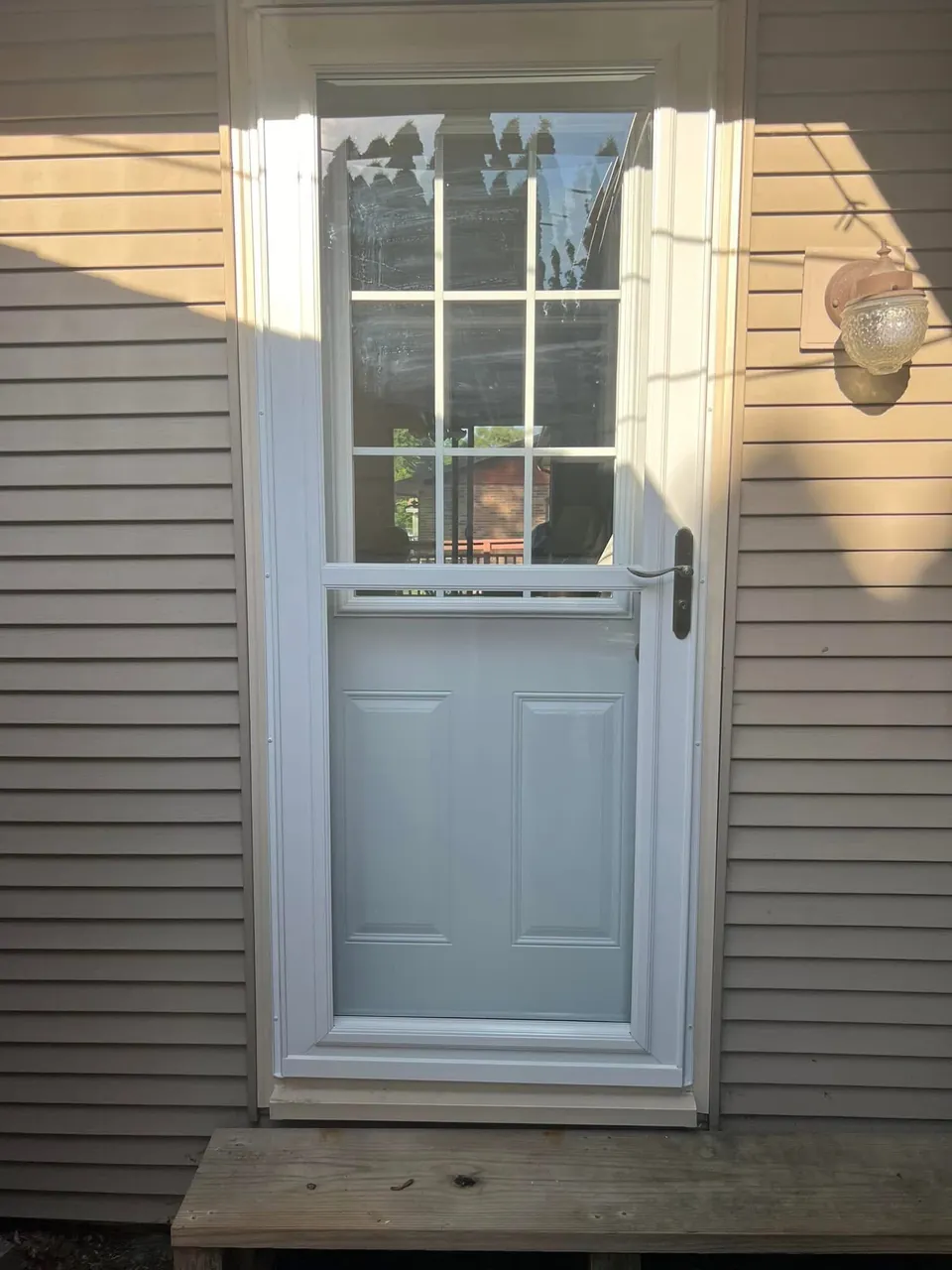 Light-colored entry door with a divided-light window and surrounding trim