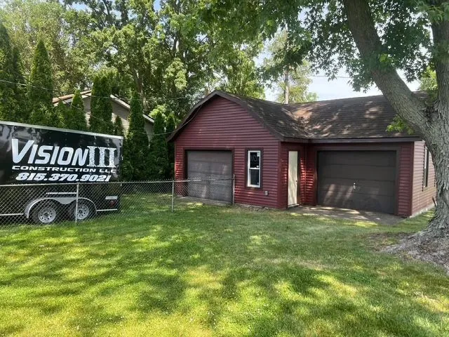 Red-sided garage with a dark roof and a Vision III Construction trailer parked beside it