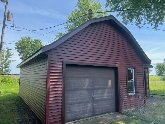 Detached garage with red siding, dark trim, and a garage door