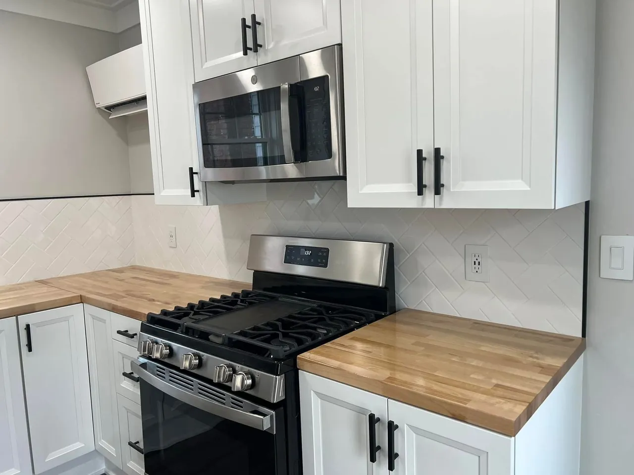 White kitchen cabinetry, wood countertops, a black range, and a stainless microwave