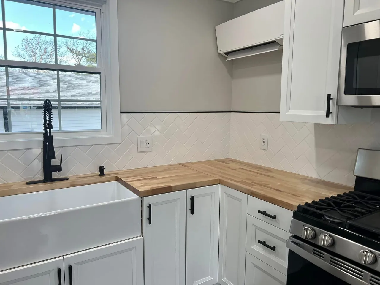 White kitchen cabinets, wood countertops, a sink beneath a window, and a black range