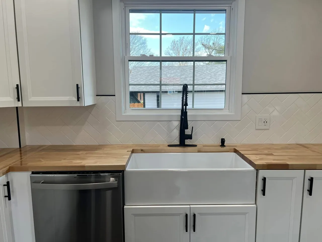 Kitchen sink beneath a window with white cabinets, wood counters, and a black faucet