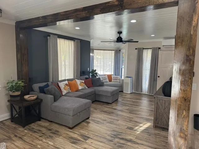 Living room with wood beams, gray seating, recessed lighting, and wood-look flooring